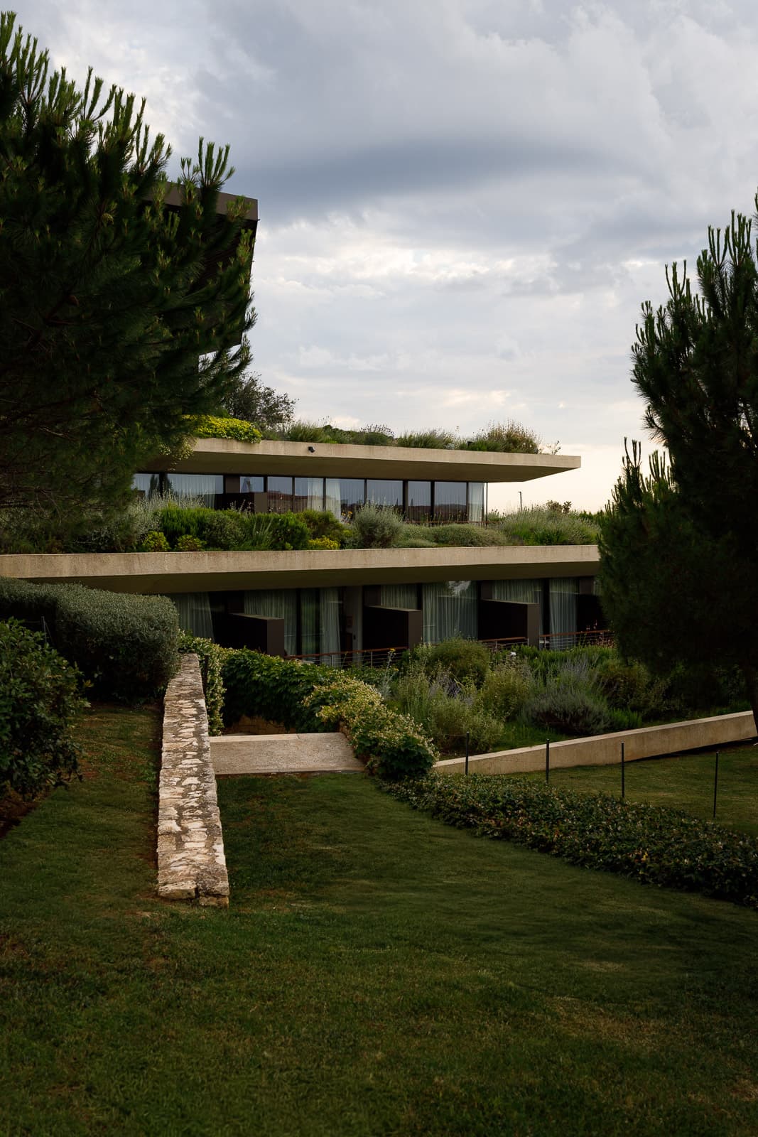 Terrassiertes Hotelgebäude mit begrünten Flachdächern und Glasfronten in mediterraner Gartenlandschaft