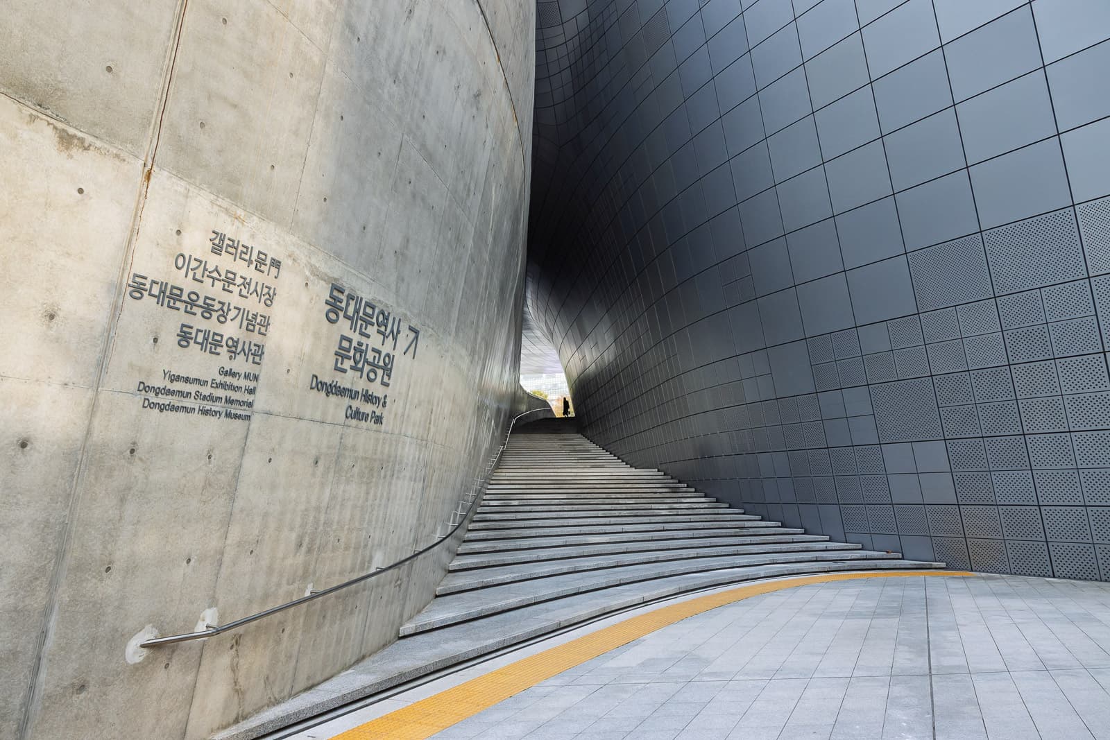 Geschwungene Freitreppe zwischen Betonwand und grauer Metallfassade am Dongdaemun Design Plaza in Seoul