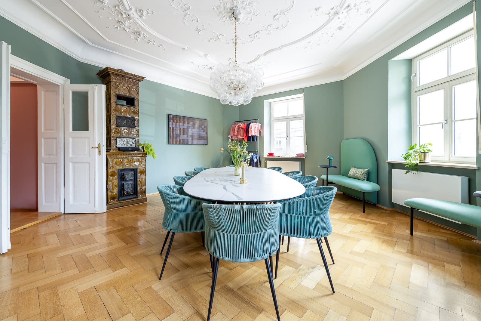 Esszimmer mit Stuckdecke, Glaslüster, ovalem Marmortisch, türkisen Stühlen und historischem Kachelofen